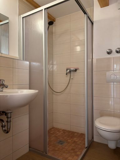 Badezimmer mit Dusche, Waschbecken und Toilette in neutralen Farben.