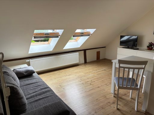 Gemütlicher Dachraum mit Fenstern, einem Sofa, Tisch und Stuhl aus Holz.