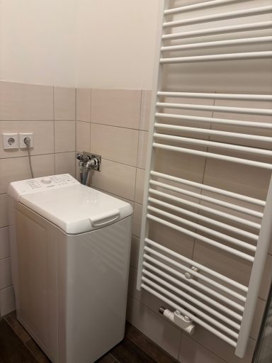 Waschmaschine neben einem weißen Heizkörper an einer gefliesten Wand.