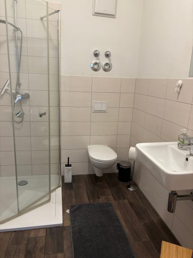 Badezimmer mit Dusche, WC und Waschbecken, mit Holzfußboden und modernen Armaturen.