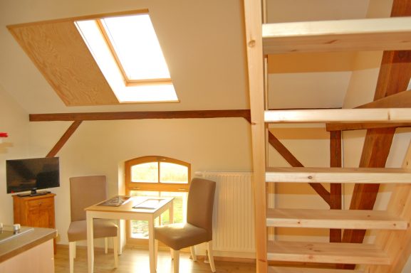 Helle Dachwohnung mit Treppe, Tisch, Stühlen und Fenster mit Oberlicht.