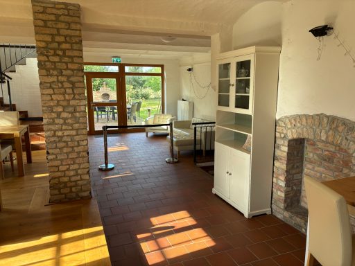Heller Innenraum mit Tisch, Stühlen, Schränken und großen Fenstern zur Terrasse.
