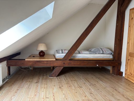Schlafzimmer mit einem Holzbett, einer Lampe und schrägen Wänden.