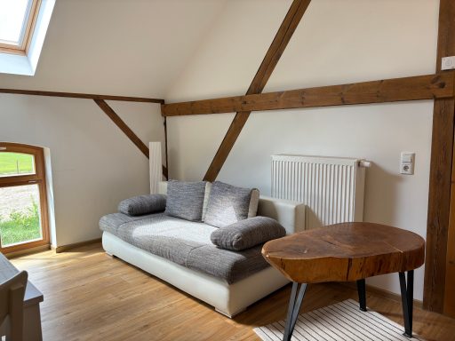 Gemütlicher Raum mit einem grauen Sofa und einem Holztisch. Helle Wände und Holzdecke.