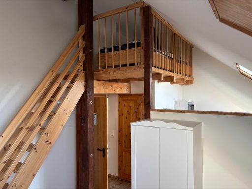 Innenansicht eines Hauses mit Holztreppe und zwei Ebenen, darunter ein Schrank.