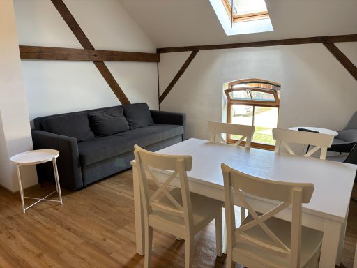 Moderner Wohnraum mit grauem Sofa, weißem Tisch und Stühlen, Holzfußboden.