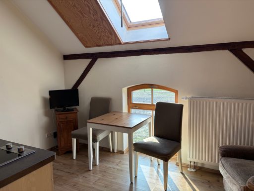 Kleinere Sitzecke mit Tisch, zwei Stühlen und Fernseher unter Dachfenster.