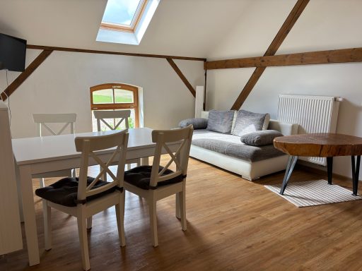 Helles Wohnzimmer mit Sofa, Esstisch und Blick durch ein Fenster auf die Landschaft.